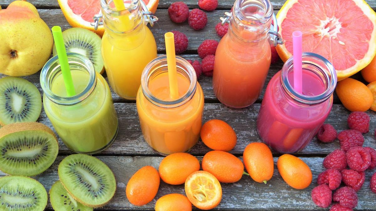 A bunch of fruits on a table with five smoothies